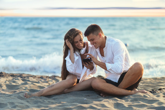 Young couple in love using smart phone on the beach 