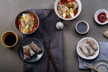 Fototapeta na wymiar Lunch with udon noodles cooked with vegetables and spring rolls. Top view. Composition with copy space on concrete background
