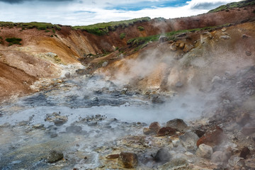 Steaming hot springs in Iceland on the background of colorful mountains