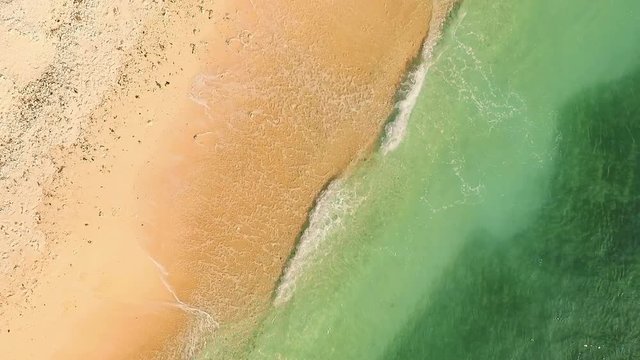 Aerial top view of clean yellow sand beach with clear water and dry corals shot with drone on sunny day.