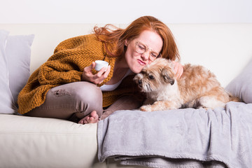 schöne, rothaarige Frau mit oranger Strickjacke schmust mit ihrem Hund
