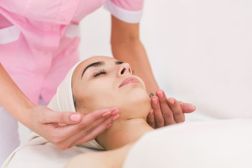 Fototapeta na wymiar Facial massage beautiful girl. Portrait of a girl in a massage parlor. Beautician doing massage of female faces. 