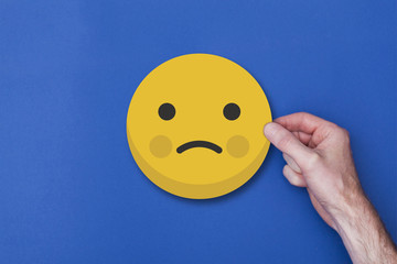 Male hand holding a emoji emoticon unhappy smiley head icon