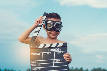 Kid playing film clapper board against summer sky background. Film director concept.