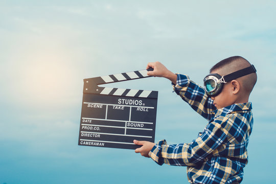 Kid playing film clapper board against summer sky background. Film director concept.