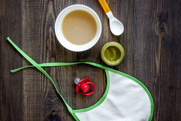 Preparing to feed baby. Puree, spoon, nipple and bib on dark wooden table background top view copyspace