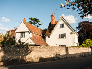 a white lovely cottage house in soft light and a brick wall and road in dedham