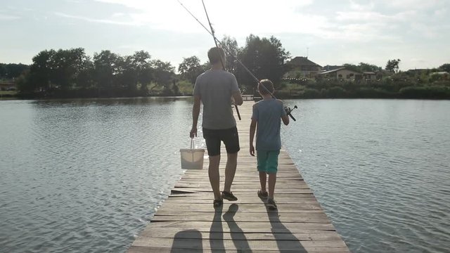 Father and son going fishing with rods on lake