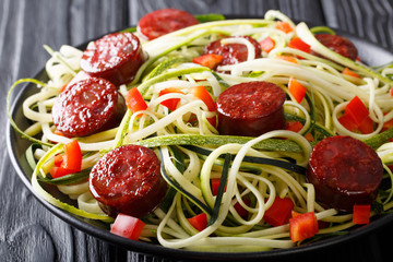 Zucchini pasta with fresh pepper and fried sausages close-up. horizontal
