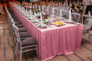 Long festive table served dishes and decorated with branches of greenery. Wedding banquet.