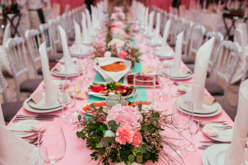 Long festive table served dishes and decorated with branches of greenery. Wedding banquet.