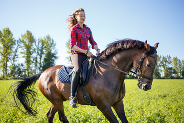 Happy young woman galloping horseback on field and enjoying feeling of freedom