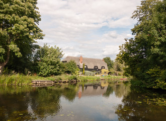 Obraz premium old english historic cottage seen over a lake with reflections