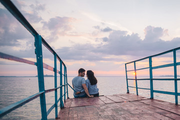lovely couple sitting on the pier and looking on sunrise