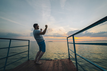 Fototapeta premium man rises hands up on the lake pier