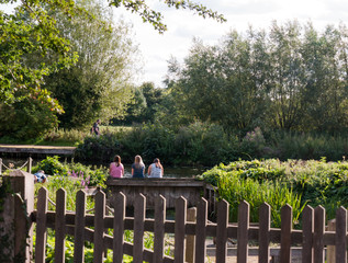 three women sitting on a wall behind fence on a summer's day