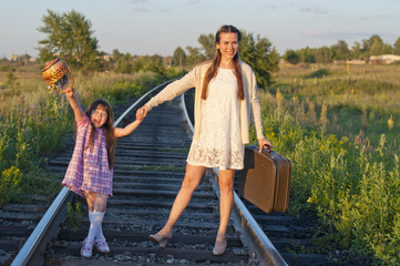 A young woman with her daughter goes by rail with a suitcase. The concept of travel. Retro style.