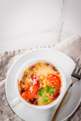 Trendy modern food, fast food, lunch in the microwave. Pizza in a mug, with ham, tomatoes, mushrooms, cheese. White cup, with a fork, on a white marble table. Copy space top view