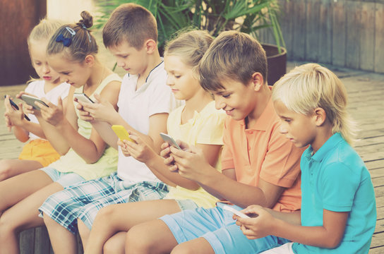 children in school age looking at mobile phones and sitting outd