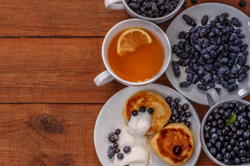 tea with lemon, cakes with sour cream, raisins, honeysuckle and blueberries on brown wooden background