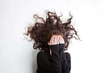 Dark haired female covering her face with her hands with her hair out around her.
