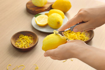 Woman taking off lemon peel with zester over table