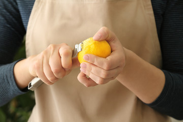 Woman taking off lemon peel with zester, closeup