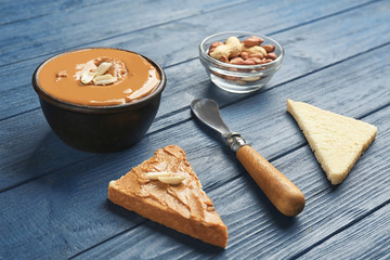 Bowl with delicious peanut butter, nuts and toasts on wooden table