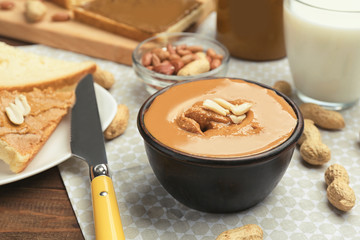Bowl with delicious peanut butter and plate with toasts on table