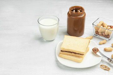 Jar with delicious peanut butter, glass of milk and toasts on light wooden table