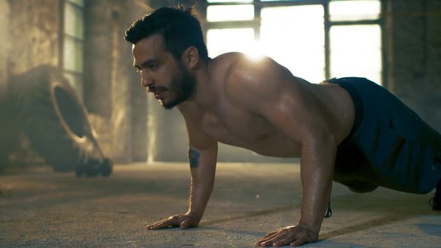 Muscular Shirtless Man Puts Heavy Effort into Doing Push-ups in a Deserted Factory Remodeled into Gym. Part of His Cross Fitness Workout/ High-Intensity Interval Training. 
