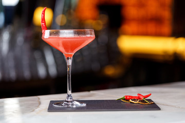 Glass of red martini decorated with chili pepper on stone