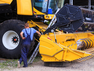 The mechanics repair the yellow Combine harvester in the farm yard. Concept theme repair, mechanics, production, industry, agribusiness company, production of food and agricultural production.
