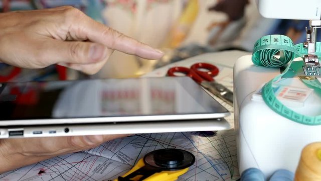 Seamstress working in her studio and browsing internet on tablet
