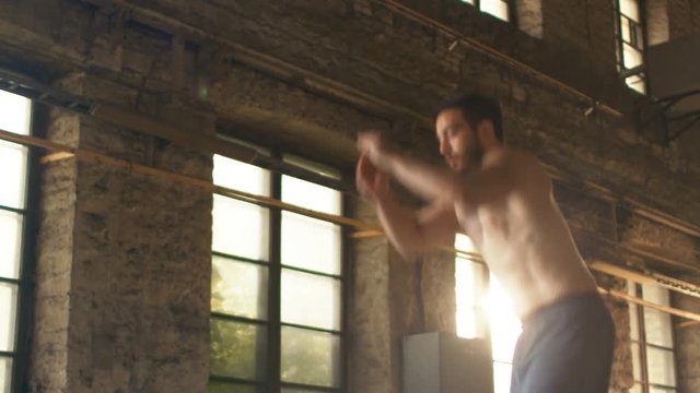 Muscular Shirtless Fit Man Energetically Box Jumps in Hardcore Gym doing Part of His Cross Fitness Training Plan. Man is Sweaty from Intense Workout/ Exercise, Gym is in Picturesque Abandoned Factory