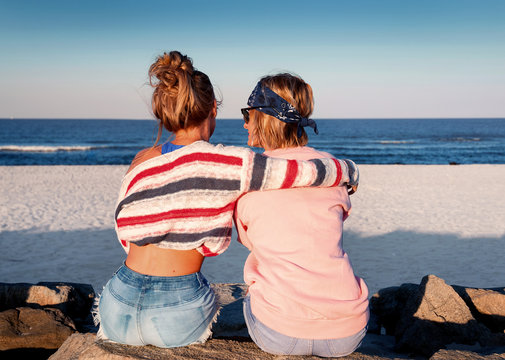 Two young girls, best friends sitting together on the beach at sunset.
