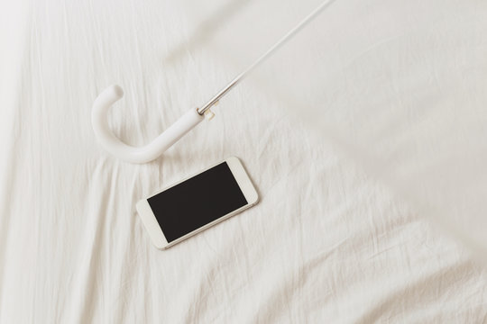 Umbrella and smartphone on white bed sheet