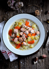 Finnish cream soup with salmon, potatoes and carrots in an old vintage plate on a wooden background. Rustic food, rustic style.