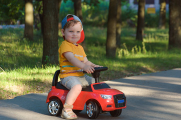 Cute little boy is riding on a red toy car on the way to the park