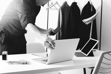 Fashion designer working with mobile phone and using laptop with digital tablet computer in modern studio