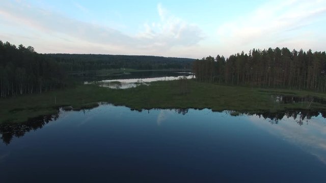 Aerial view of beautiful landscape in North Sweden. Flying up over forest and tranquil lake, reflections in the water