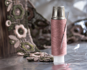 Coil of pink thread and thimble against the background of pink and gray lace. Conceptual photo - peaceful warrior.