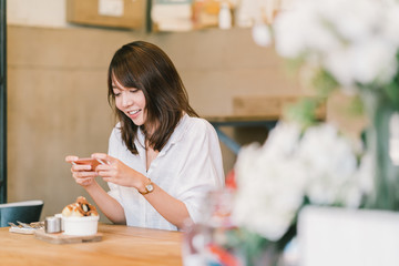 Beautiful Asian girl taking photo of sweet desserts at coffee shop, using smartphone camera, posting on social media. Food photograph hobby, casual relax lifestyle, modern social network habit concept