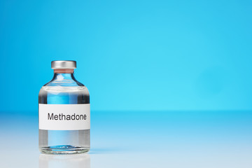 A ampoule of methadone stands on white surface against blue background on the left. (English...