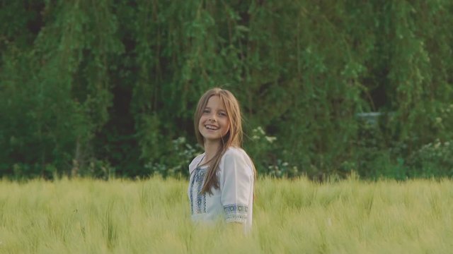 Happy young girl walks and poses in the green wheatfield. Slowly
