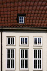 Fototapeta na wymiar Rote Dachziegel und hohe Fenster / Ein altes Gebäude mit markanten glänzenden roten Dachziegeln und hohen Fenstern.