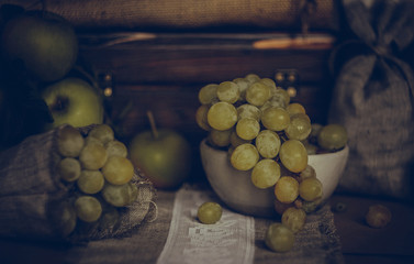 Fresh green grapes and green apples on a  textile napkin on old wooden background. Rustic style. Selective focus. Vintage style stylized photo.
