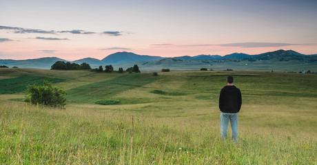 Man standing in the meadow, watching colors of the sunrise