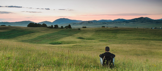 Man sitting in the meadow, watching colors of the sunrise