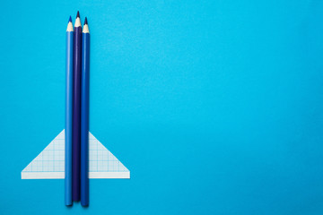 Airplane made of pencils and paper on a blue background. Space for text.